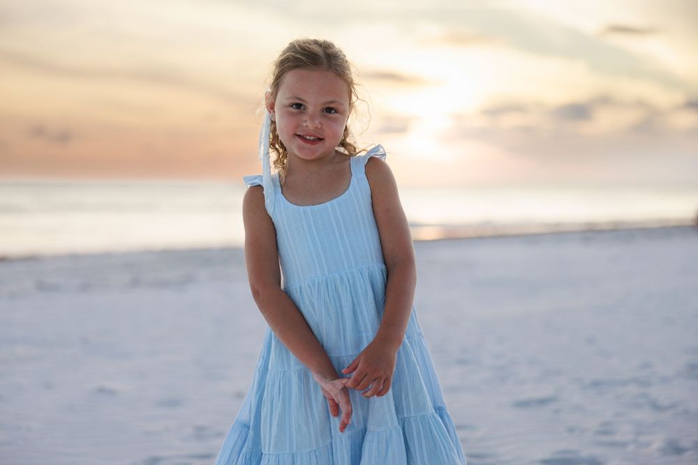 A series of seaside photos shows someone in a light blue dress walking and posing on a sandy beach at sunset.