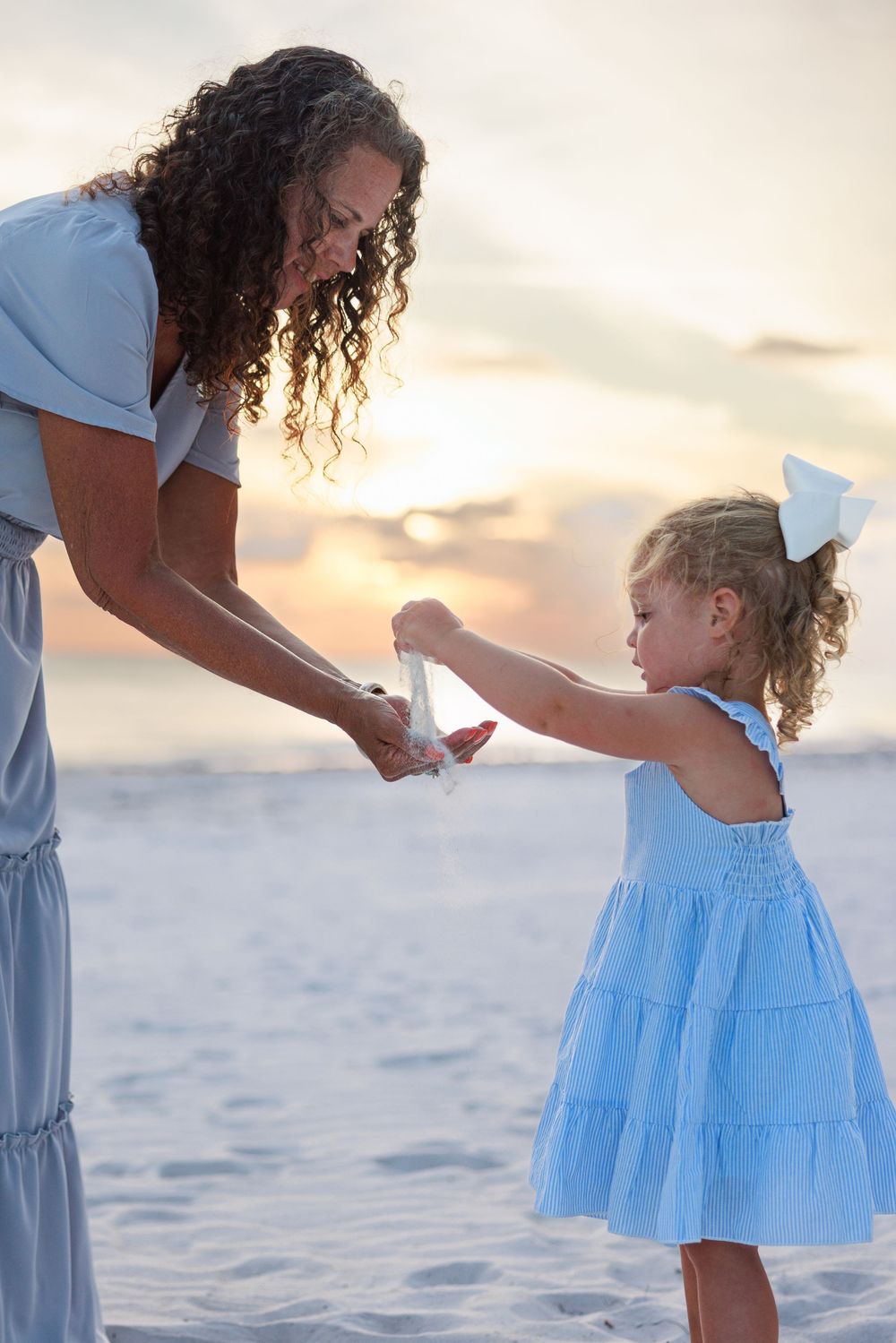 Four sequential photos show a loving moment between a parent and child in blue and white outfits on a beach at sunset.
