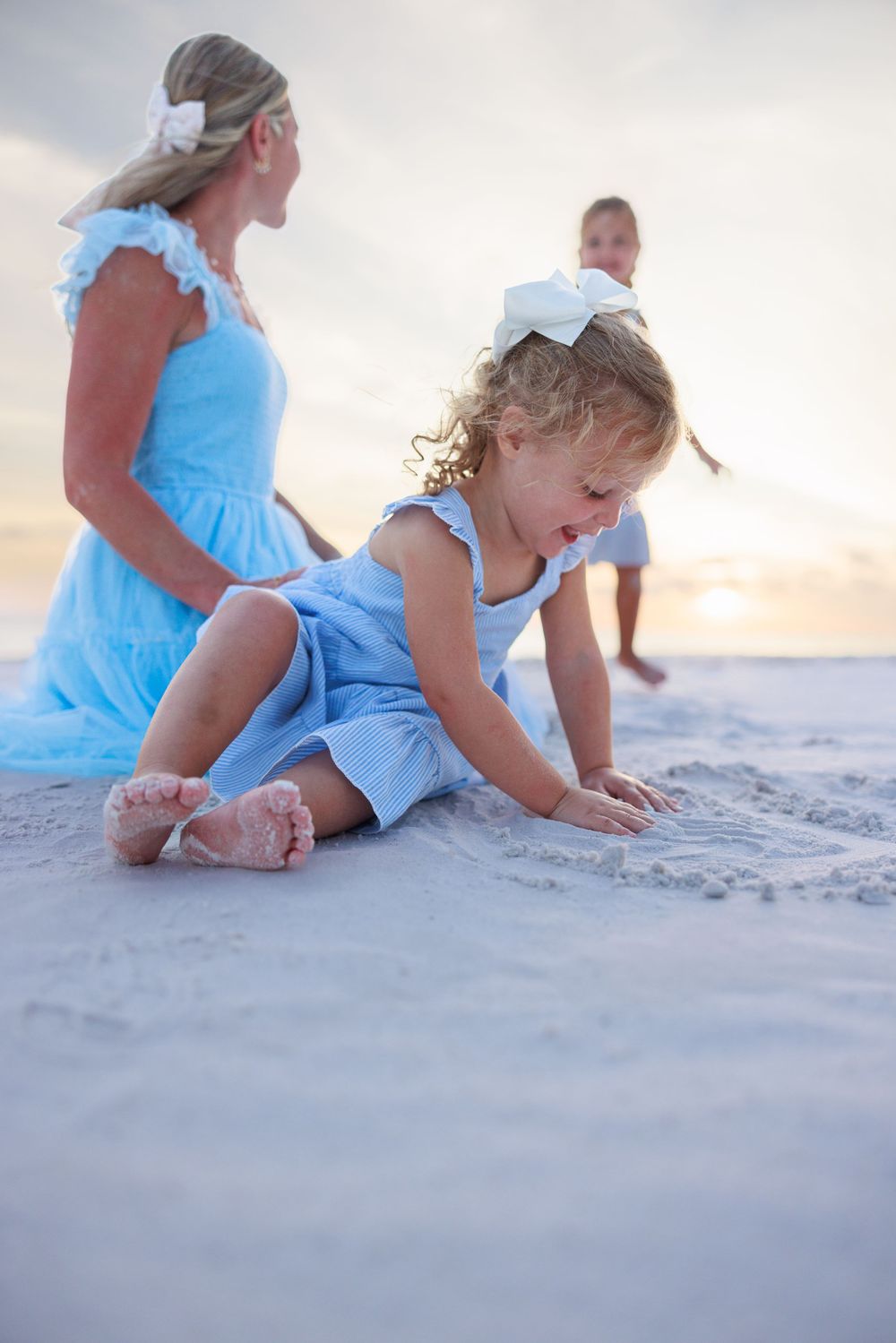 People in coordinating blue dresses spend time together playing in the sand at sunset on the beach.