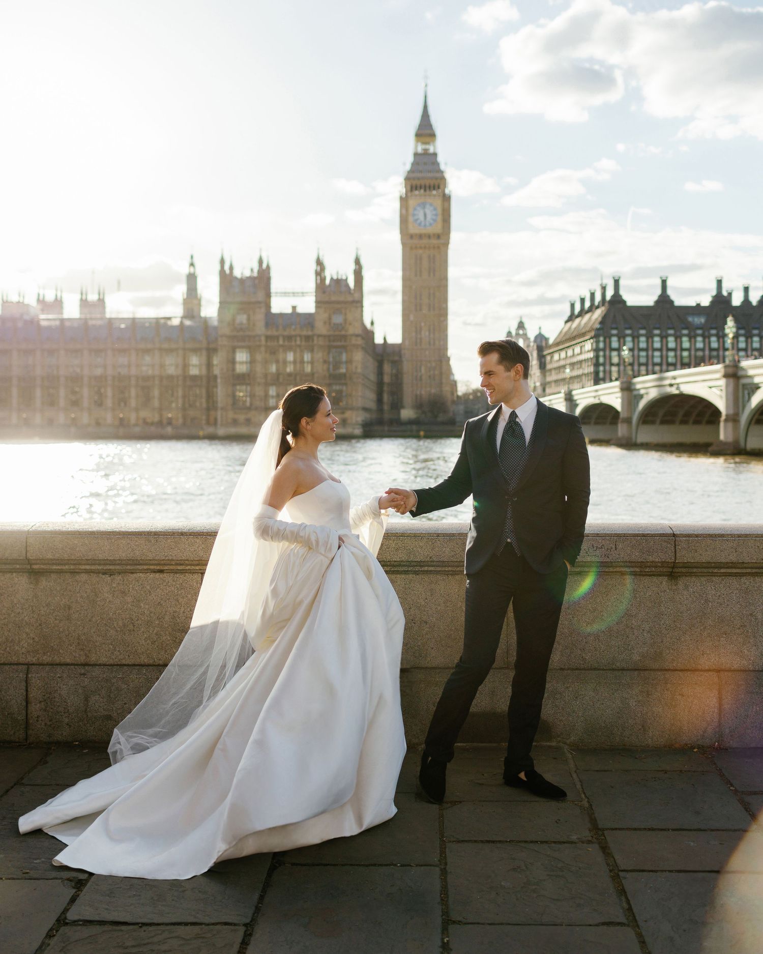 Bride and groom holding hands, smiling at each other, with the iconic Big Ben and the river Thames in the background.