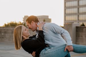 A romantic couple embraces and leans in close together on a rooftop at golden hour.