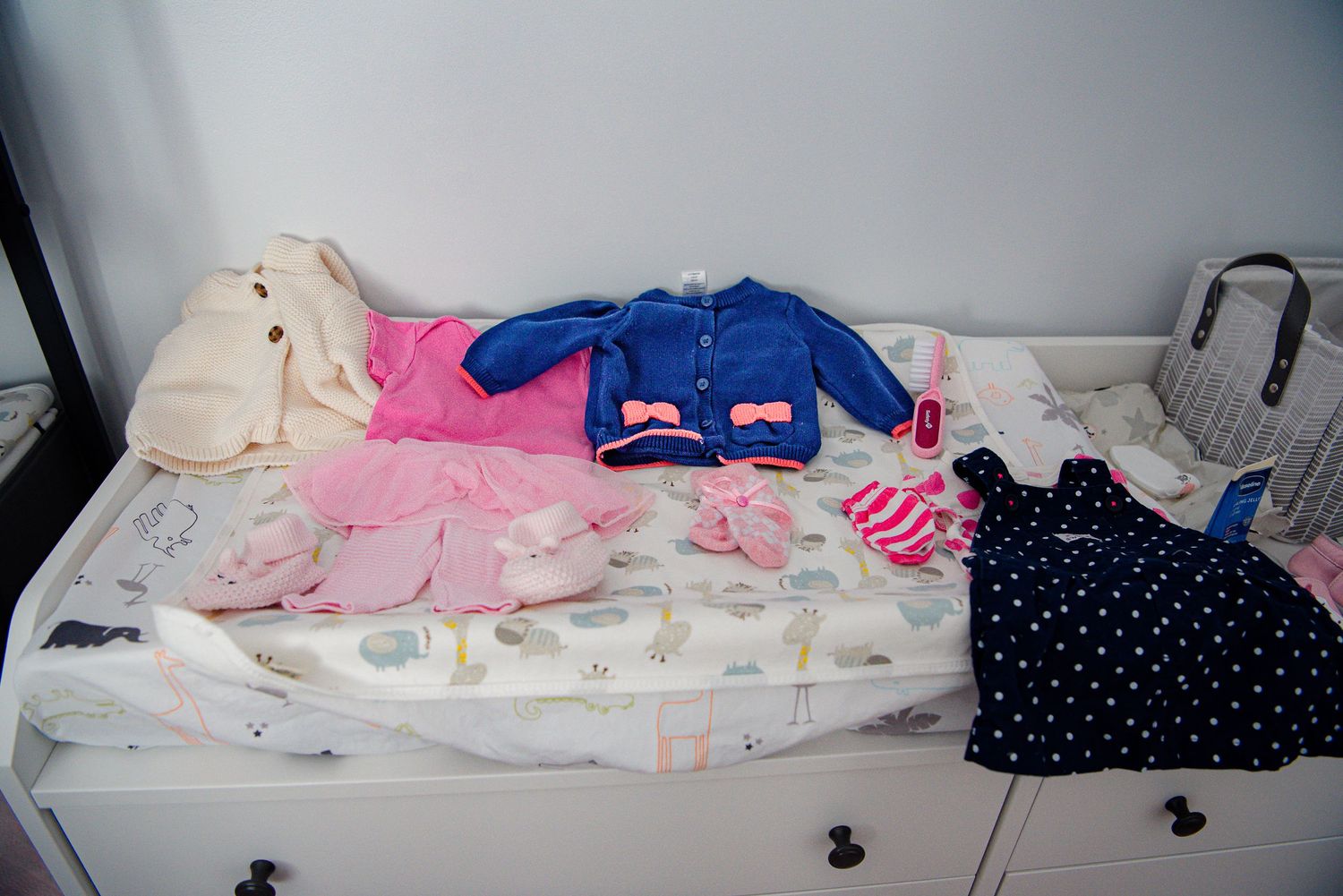 Various baby clothes and garments laid out on white surface including pink, blue, and polka dot items.