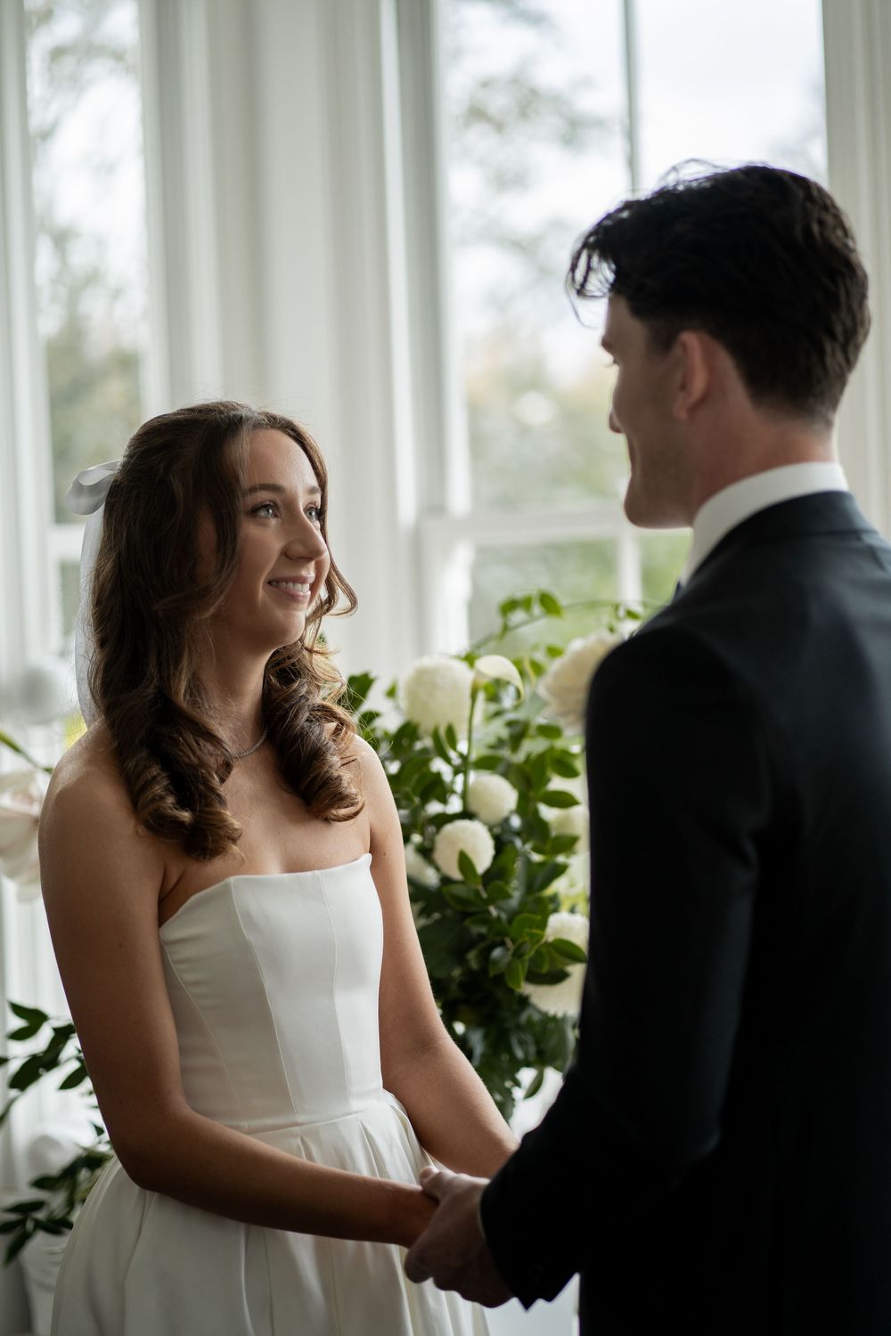 Intimate wedding moment shared between couple in bright indoor setting with greenery and windows.