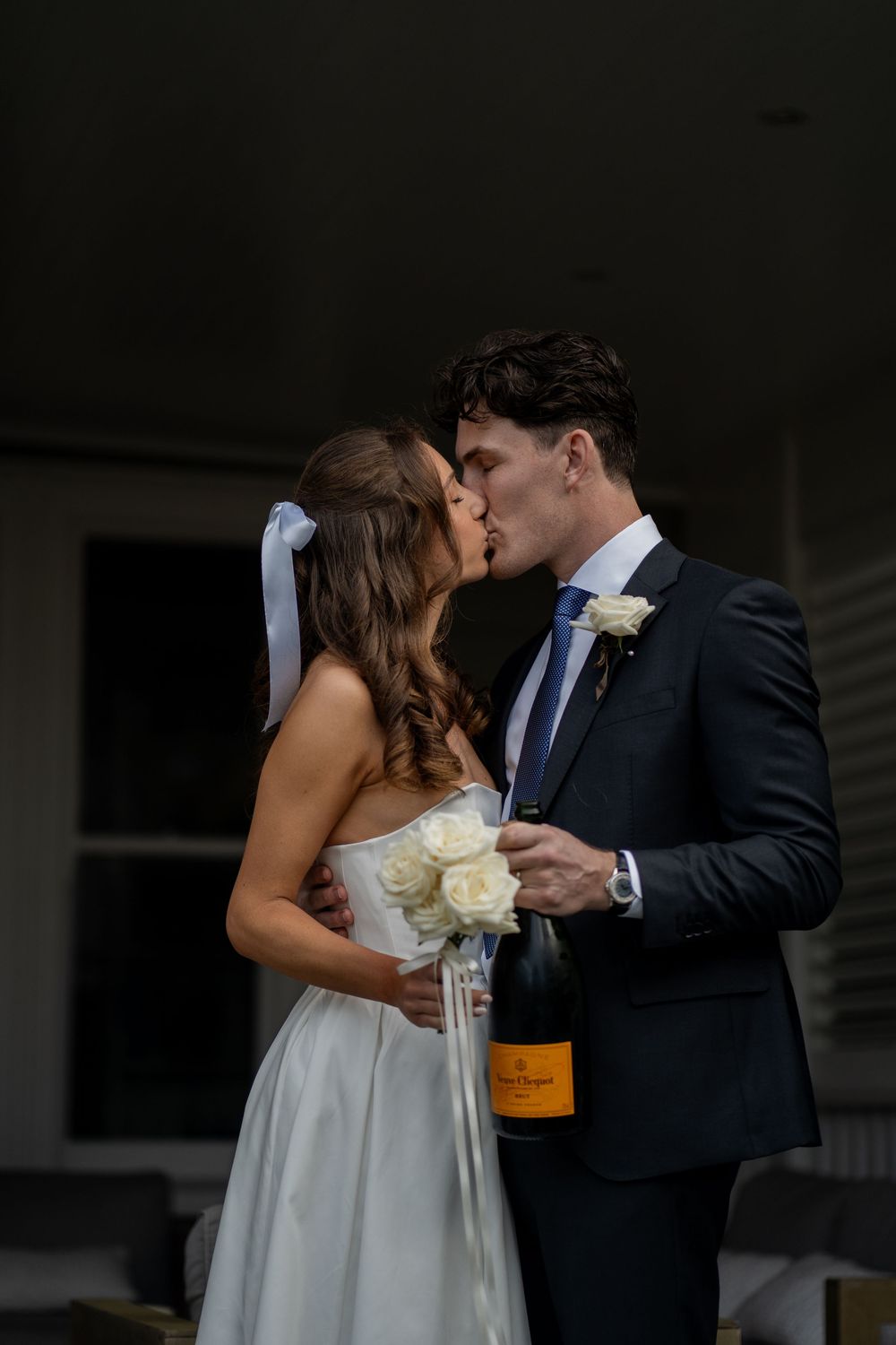 Romantic wedding couple sharing champagne and kisses in dark moody setting.