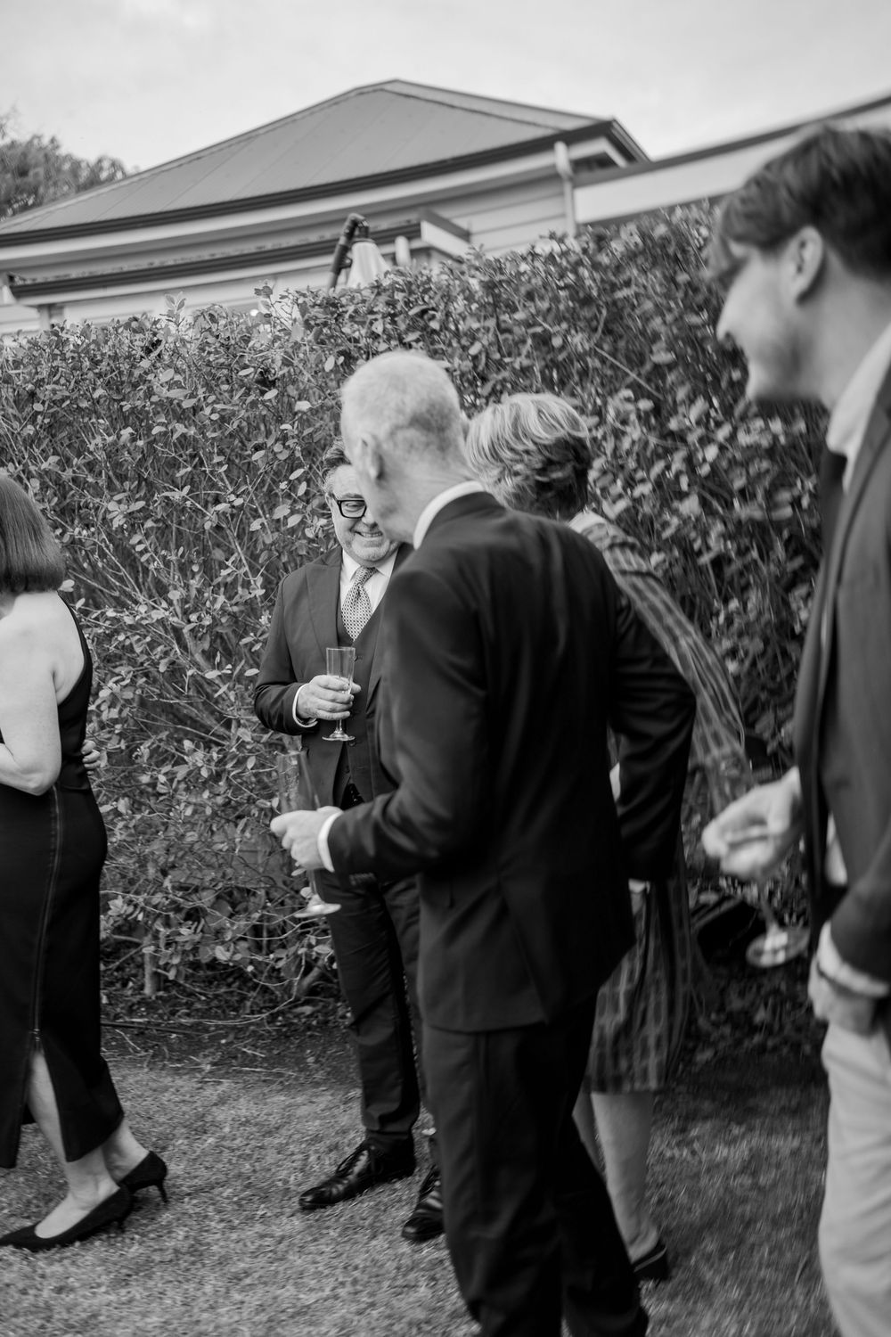 Wedding guests in formal attire mingling outdoors during reception celebration.