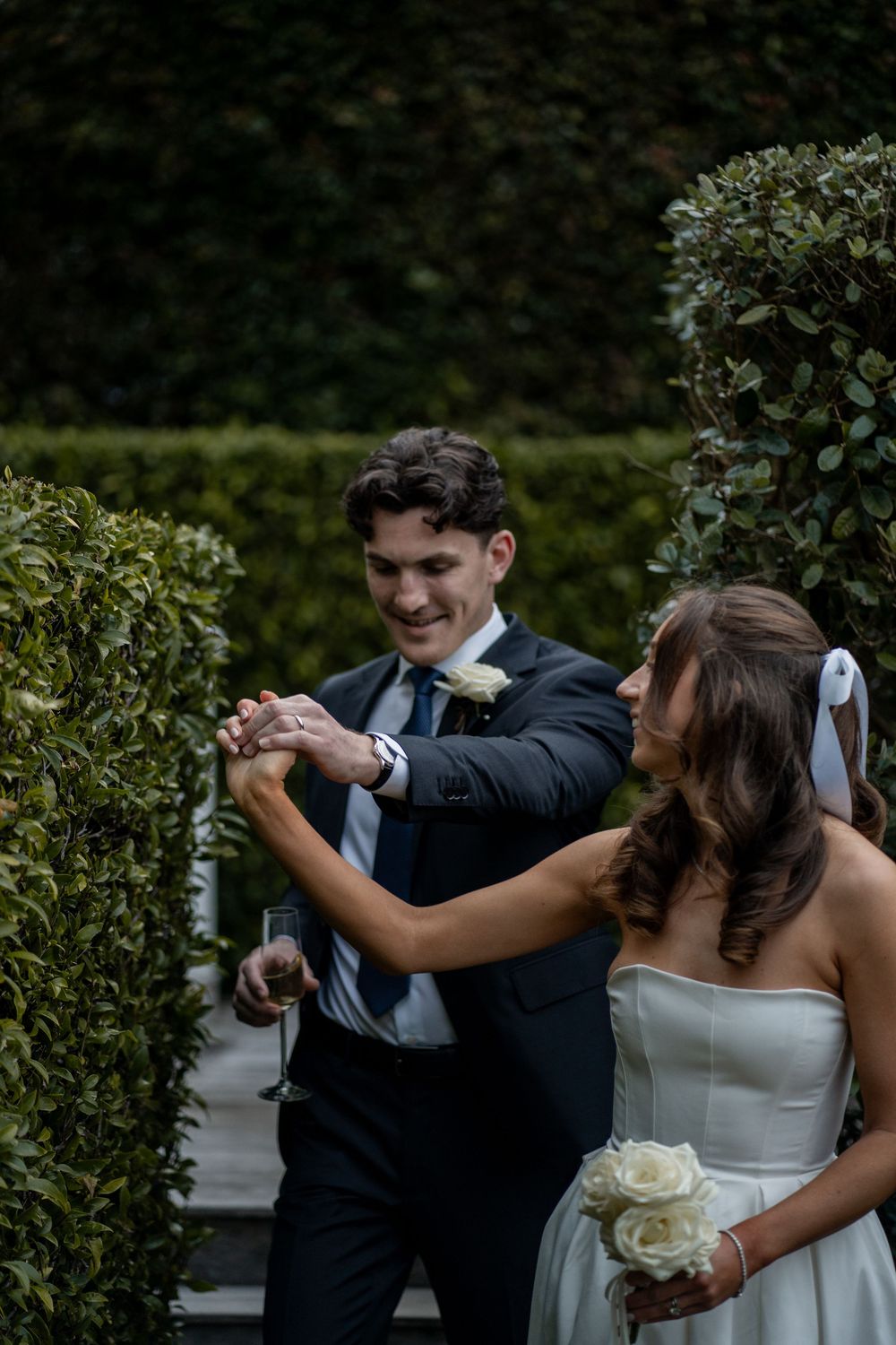 Couple in wedding attire dancing and embracing in garden setting.
