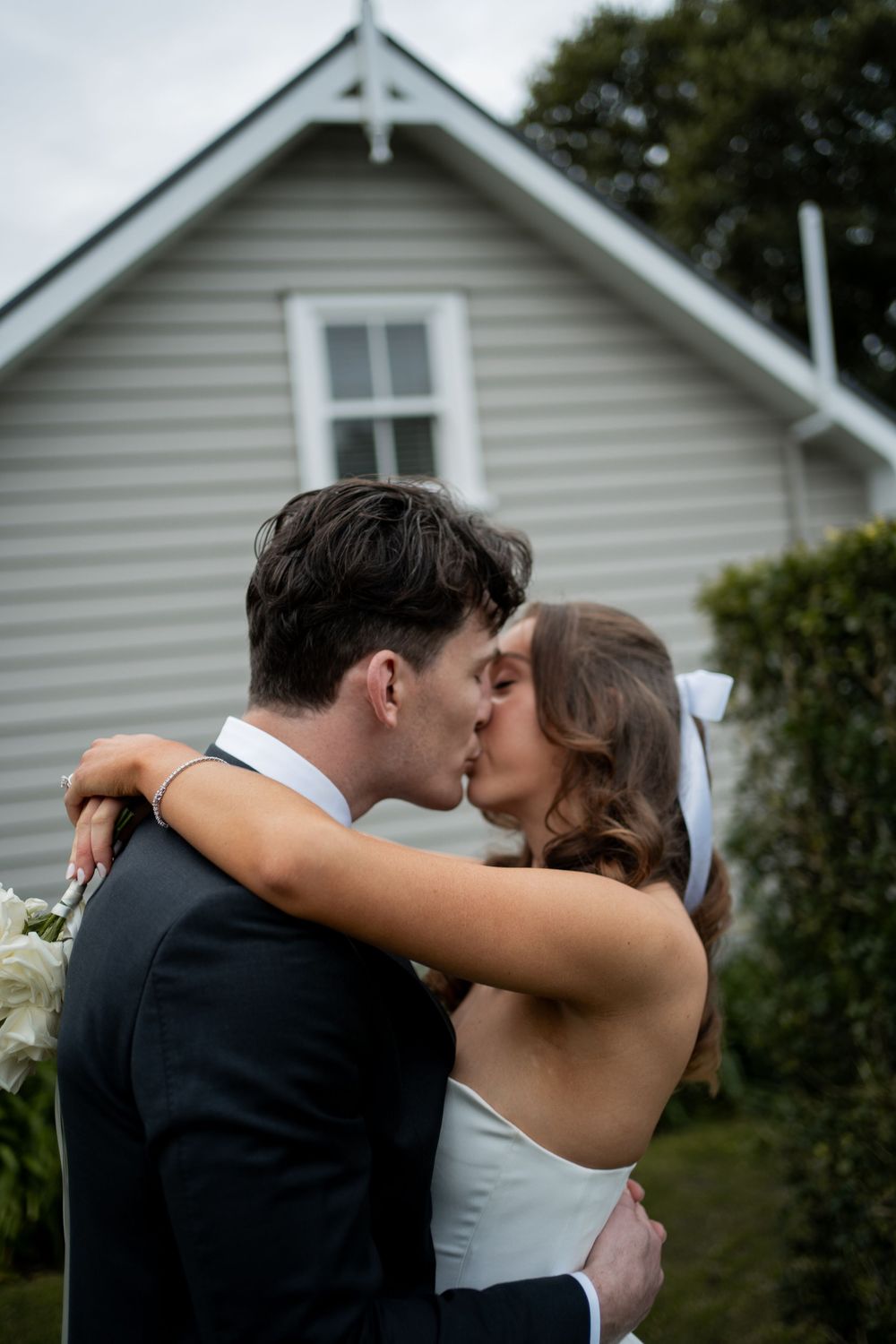 Wedding couple sharing intimate moments outside white house with gabled roof.