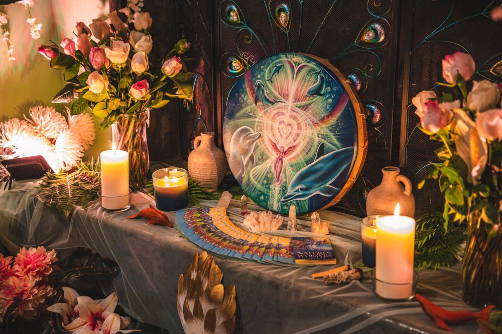 Mystical altar setup with glowing candles, floral arrangements and peacock-themed artwork in dim lighting.