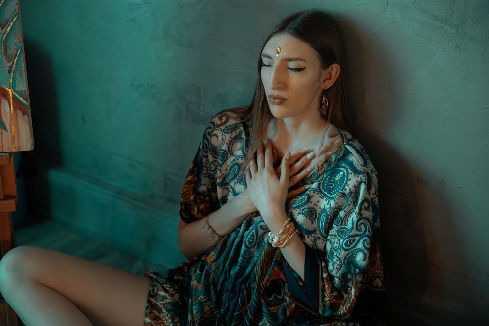 Moody portrait in teal lighting with ornate floral kimono against textured wall.
