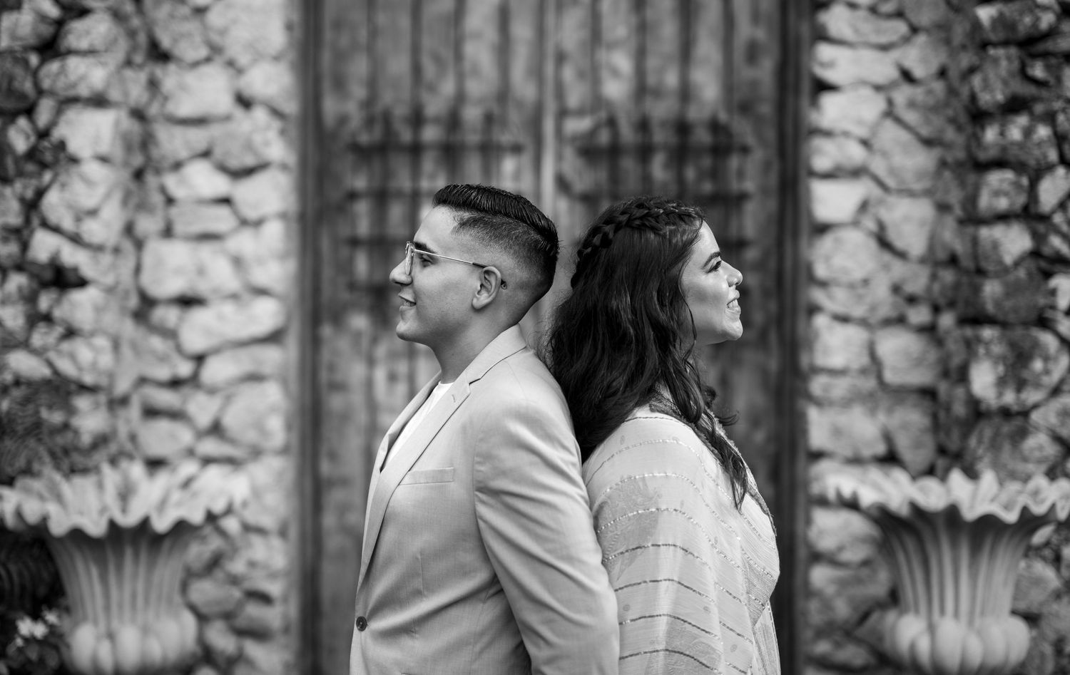 A romantic black and white photo series showing a couple embracing outdoors against a stone wall backdrop.