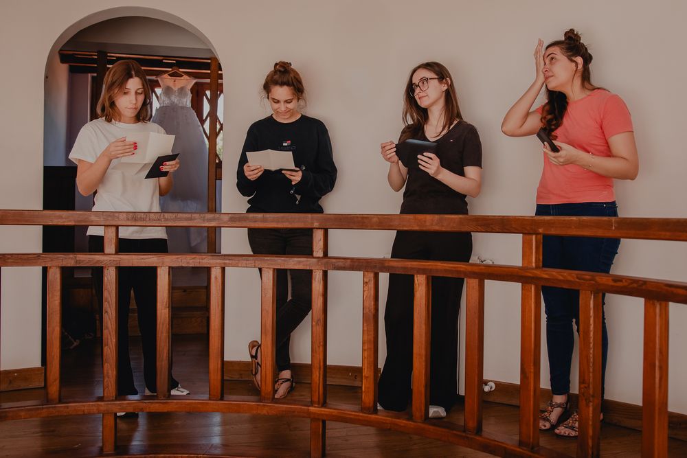 Four people standing along a wooden railing while looking at their phones.