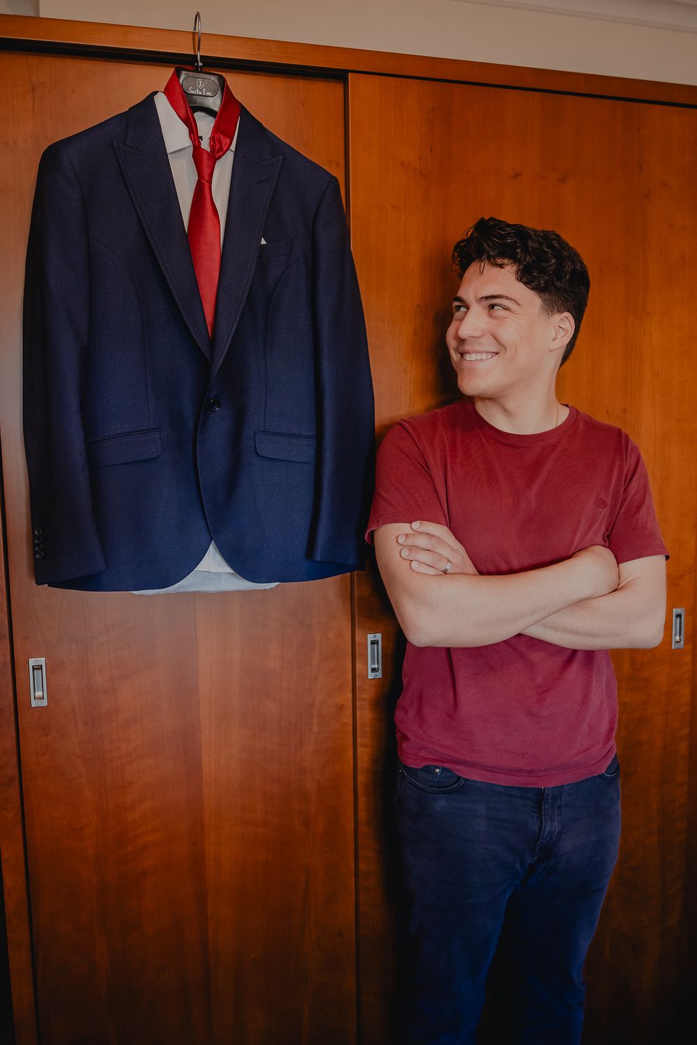 A navy suit jacket with red tie hangs on display against wooden closet doors.