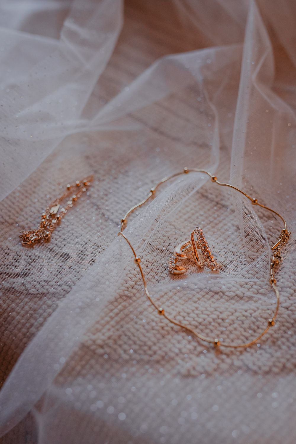 Delicate rose gold jewelry and earrings laid out on white tulle fabric.