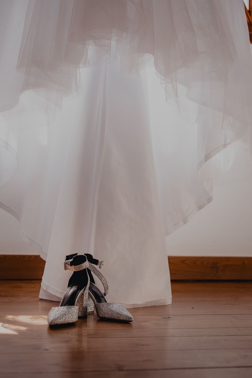 Sparkly silver bridal shoes placed beneath the hem of a flowing white wedding gown.