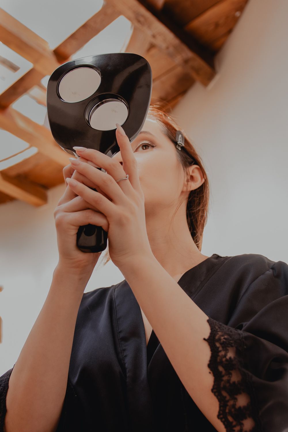 Person in black robe looking into compact mirror during wedding preparations.
