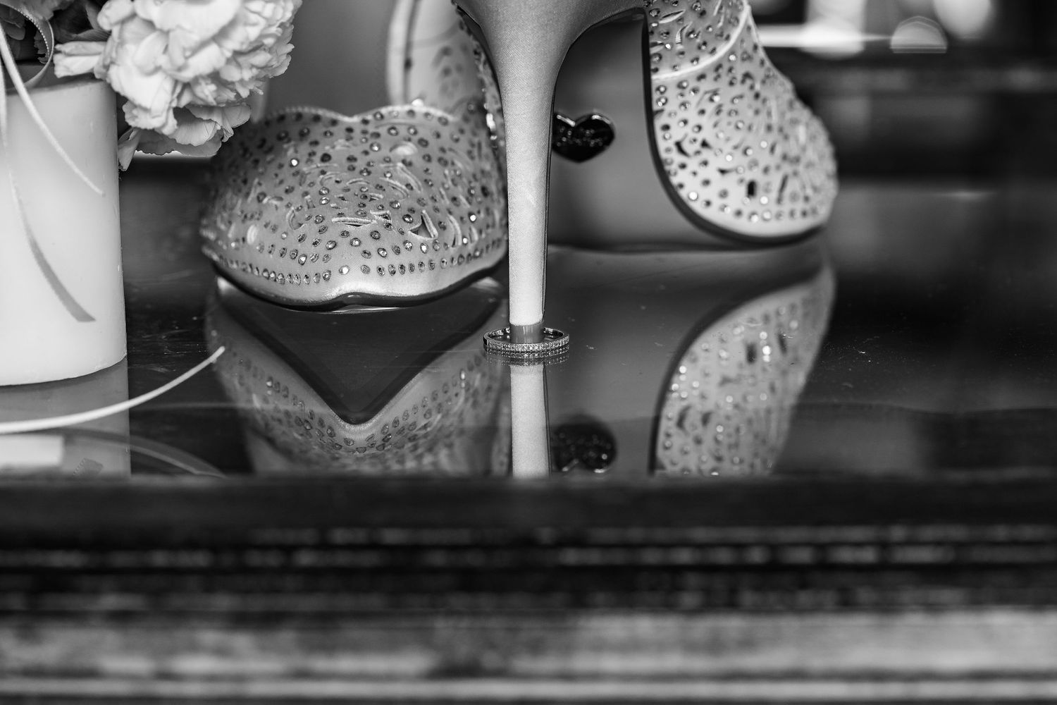 Sparkly bridal shoes reflected on glossy black surface in black and white photography.