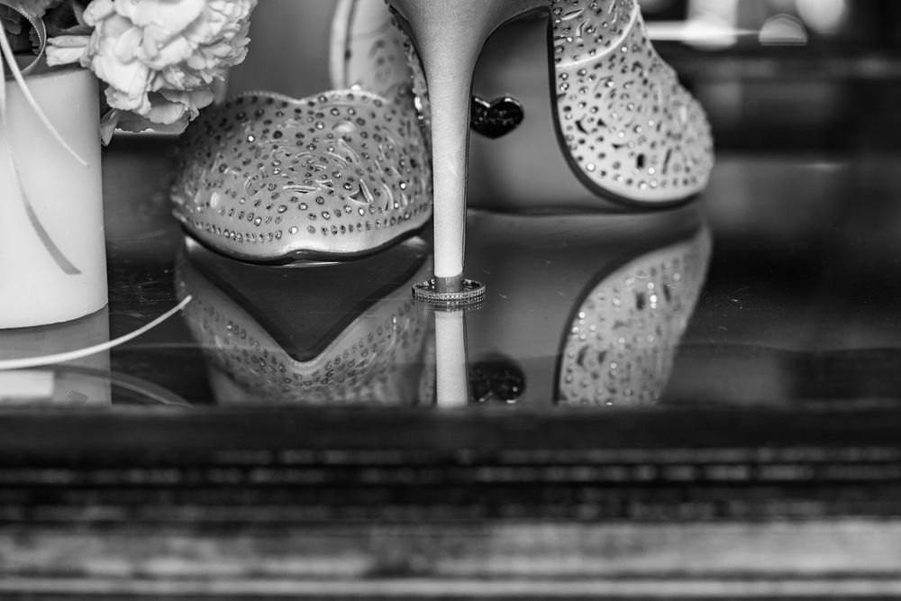 Sparkly bridal shoes reflected on glossy black surface in black and white photography.