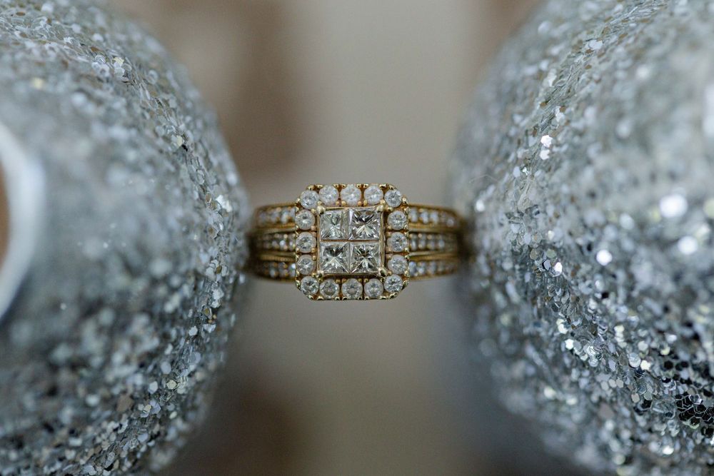 Gold diamond engagement ring with multiple stones photographed between sparkly surfaces.