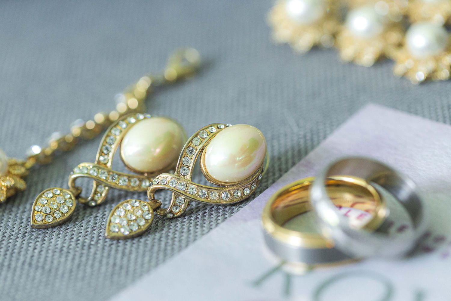 Pearl and diamond jewelry set with wedding rings arranged on gray fabric.