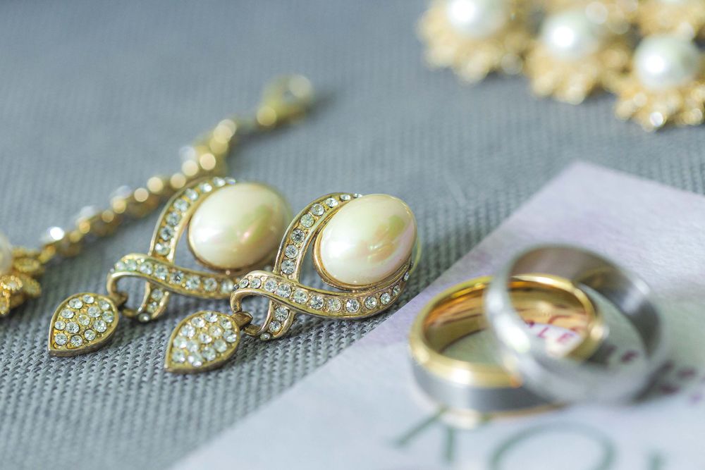 Pearl and diamond jewelry set with wedding rings arranged on gray fabric.