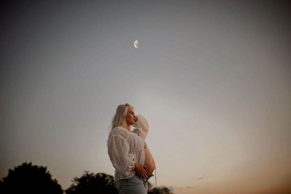 A silhouetted couple shares an intimate moment under a crescent moon during golden hour.