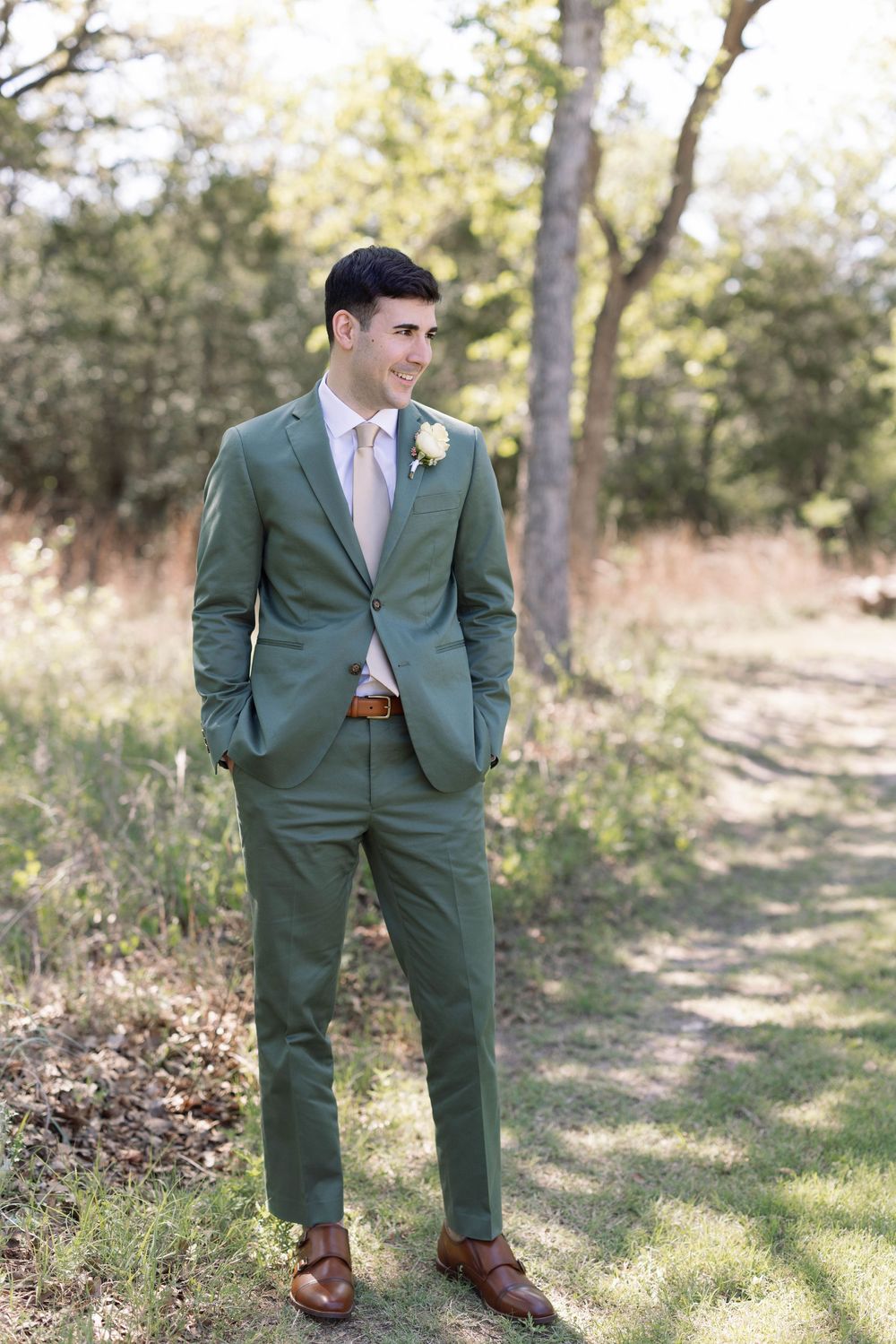 Stylish wedding attire featuring green suit with brown leather shoes in an outdoor woodland setting.