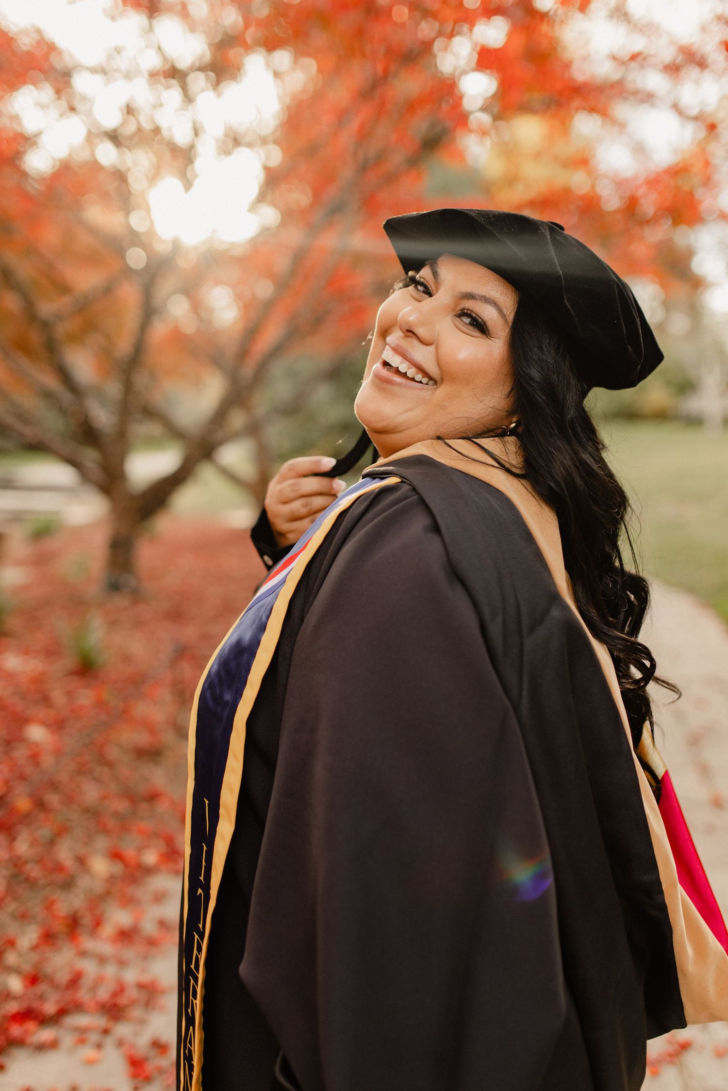 Graduate in cap and gown poses with joyful expressions among fall foliage in Wheaton Maryland