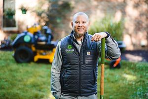 Candid outdoor shot of service worker in vest smiling with equipment visible behind.