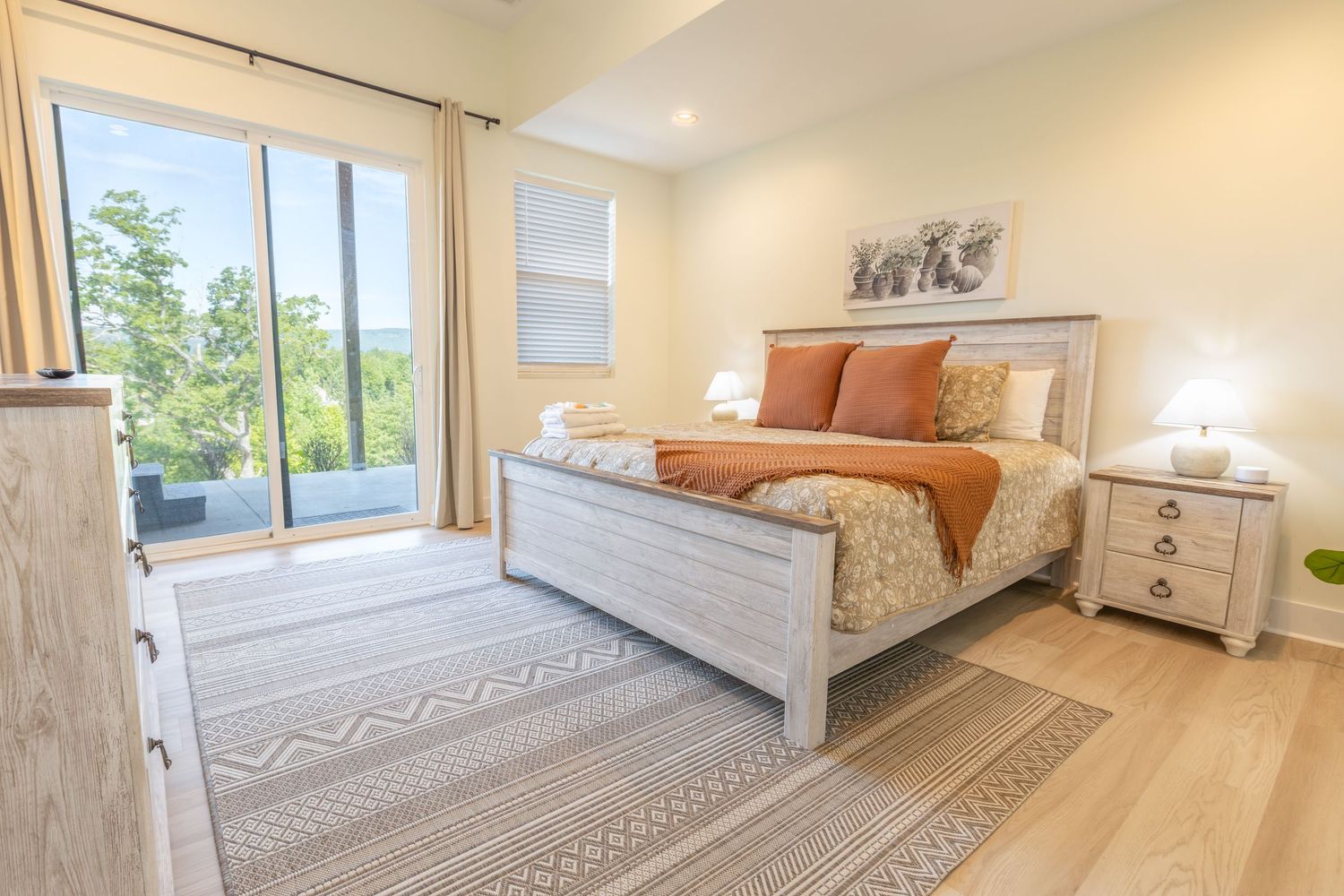 A bright and airy bedroom with white bedding, hardwood floors, and modern coastal decor showcases sunlight through windows.