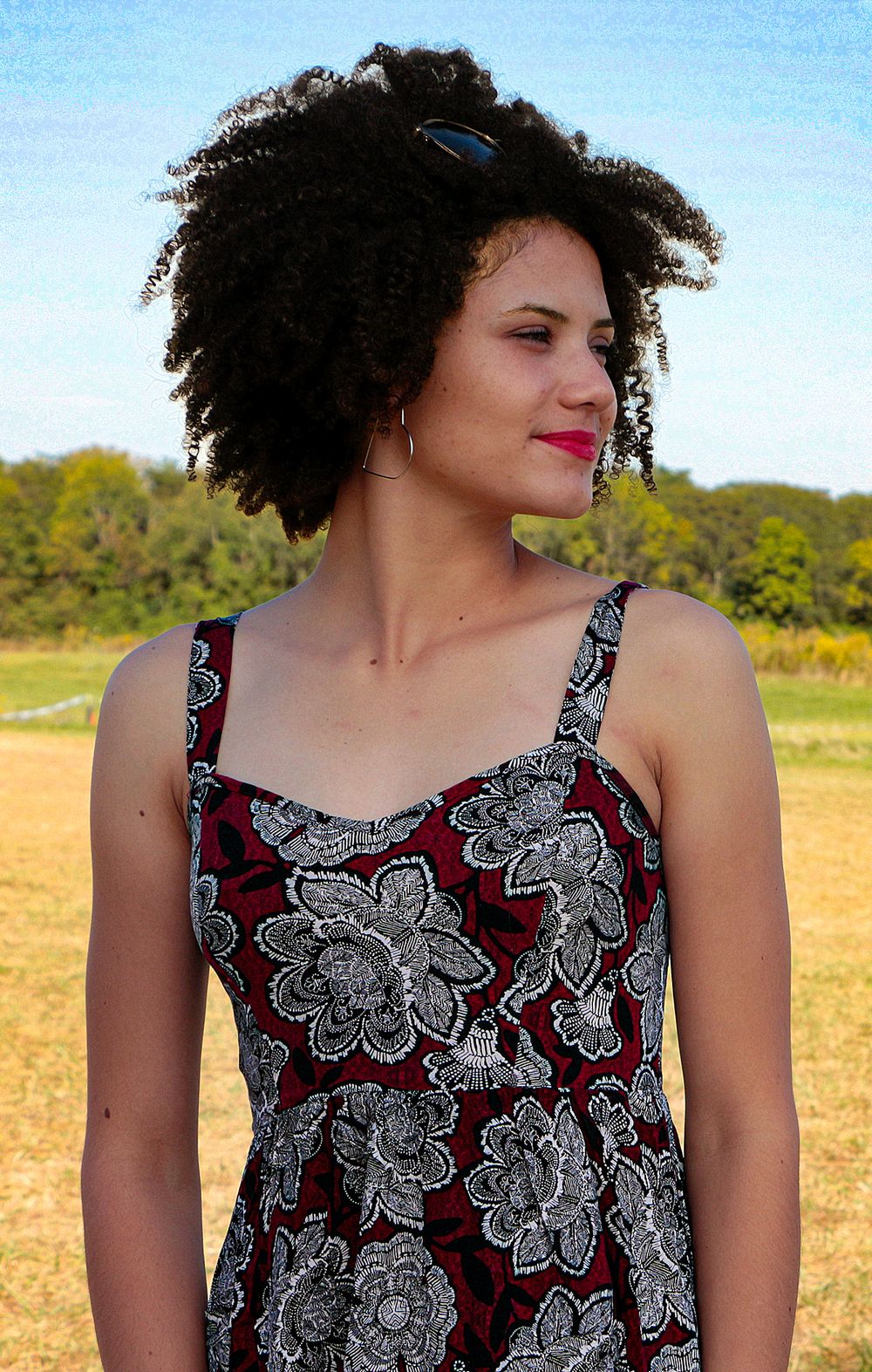 Girl with natural curly hair wearing a burgundy floral print sundress against a sunny outdoor backdrop.