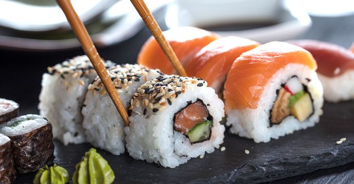 Fresh sushi rolls with salmon, cucumber and avocado served on a black slate plate with chopsticks and wasabi.