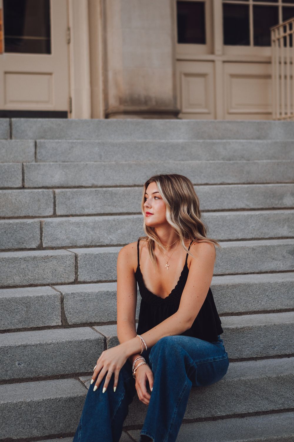 A person in a black tank top and jeans sits thoughtfully on concrete steps in an urban setting.