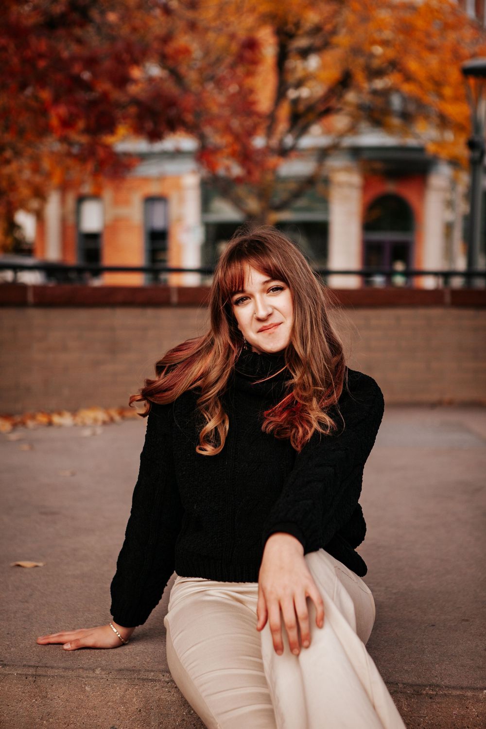 A figure in a black sweater lies casually on wooden steps surrounded by autumn trees with orange foliage.
