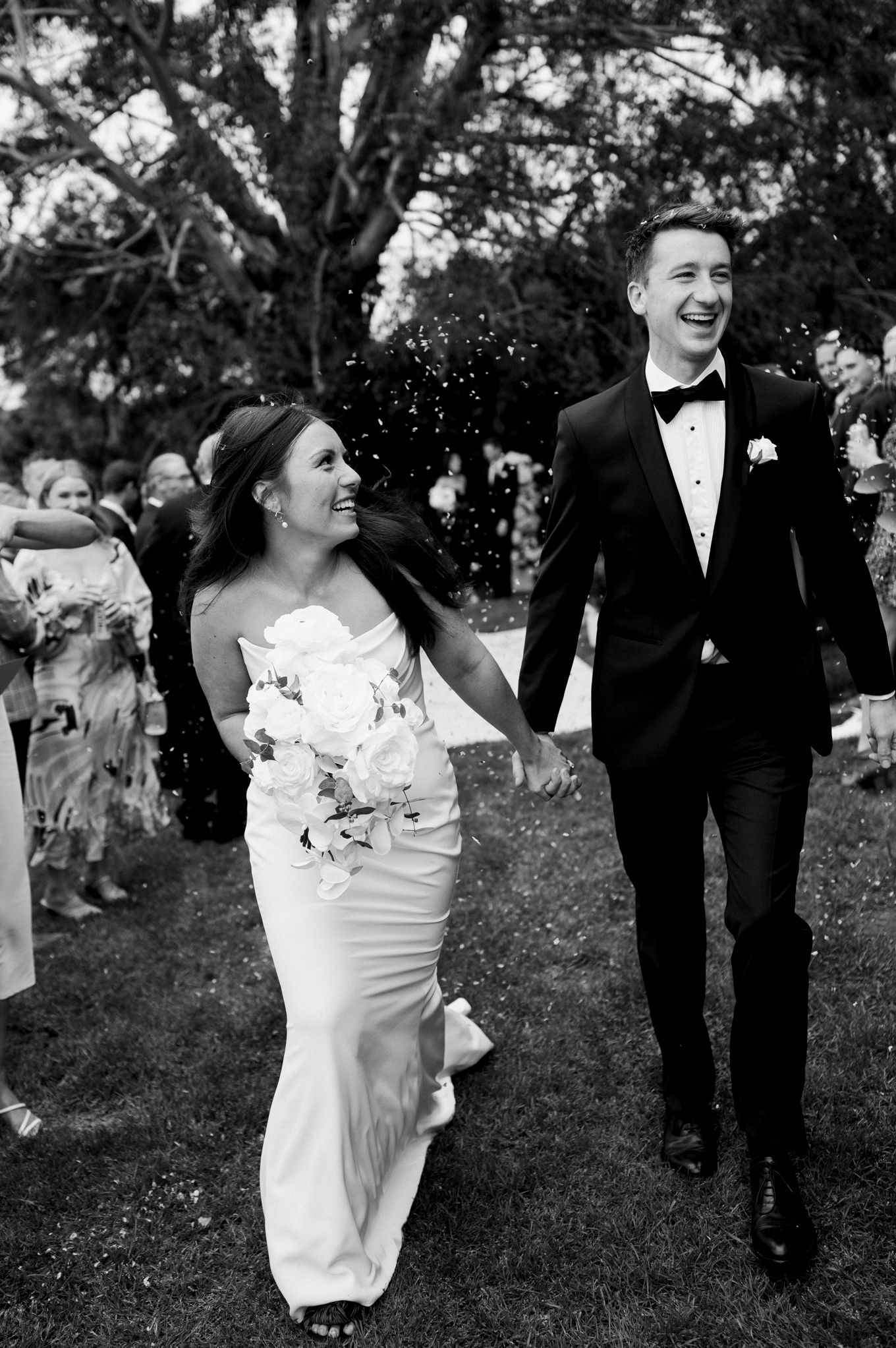 Joy-filled black and white wedding exit photo with confetti on garden path.