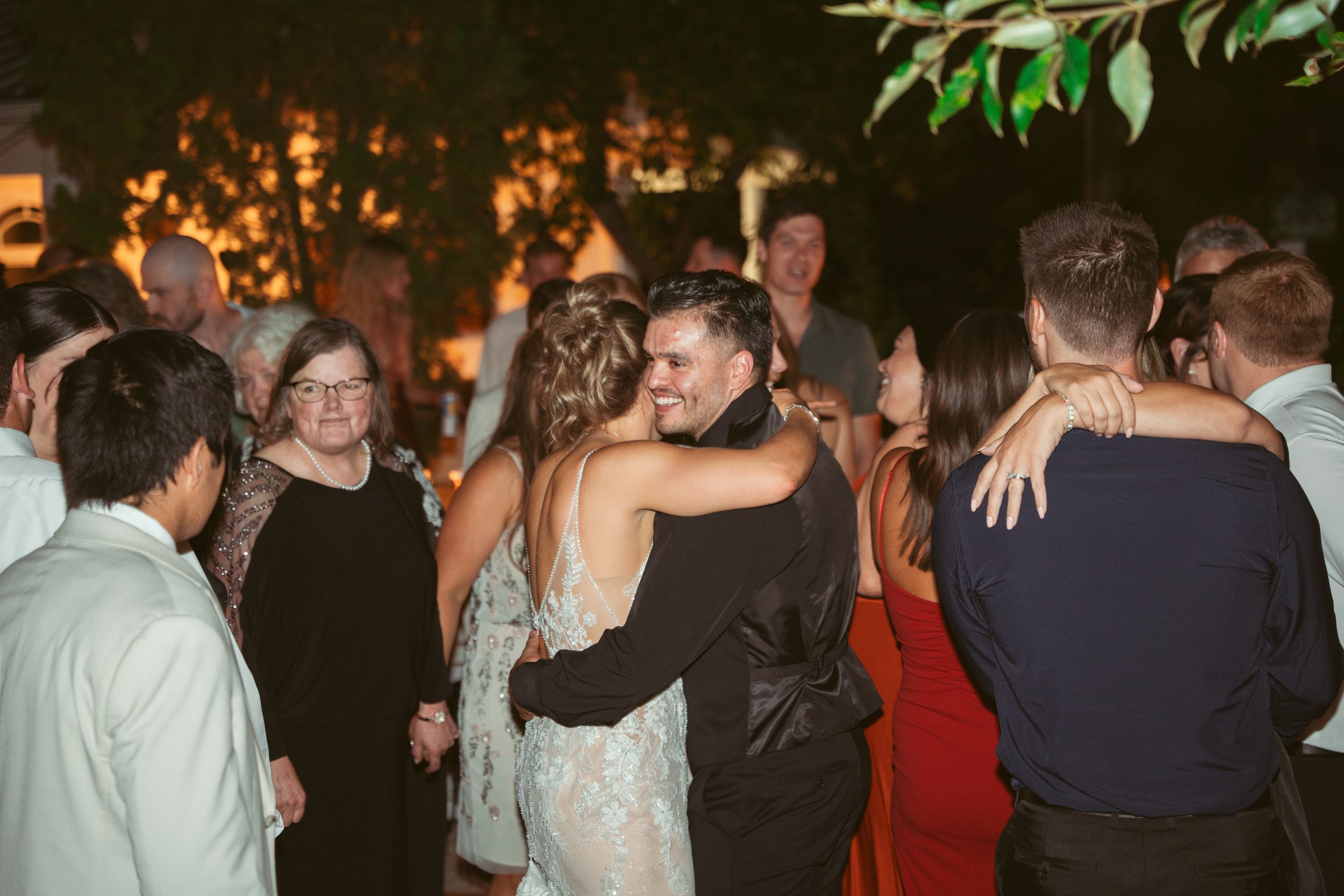 Party guests dancing together at a dimly lit evening celebration with decorative lights.