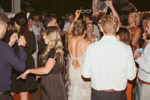 Crowd dancing at a wedding reception party under warm lighting with string lights overhead.