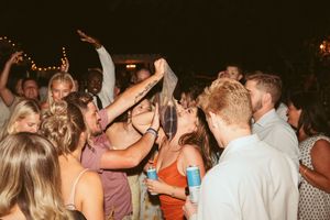 People dance and celebrate at a festive nighttime party with dimmed lights and string decorations in the background.