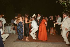 Guests dance together at an outdoor evening wedding reception with some wearing orange dresses and white suits.