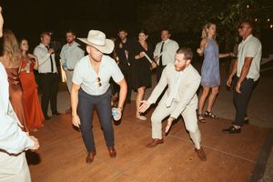 Two wedding guests dance energetically on a wooden dance floor at a reception as other guests watch from the sides.