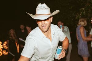 Person in white cowboy hat is seen dancing and socializing at a nighttime party event.