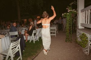 A bride in a white lace dress dances at an outdoor reception with white chairs in the background.