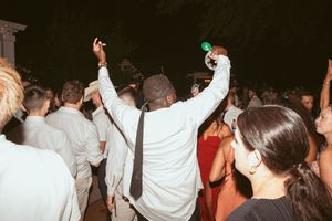 Wedding party guests with raised arms dancing enthusiastically during nighttime celebration.