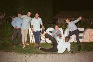 Wedding party members posing playfully with letters spelling 'Mr & Mrs' during nighttime celebration.