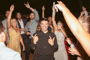 Party guests dancing and raising their hands in celebration at a nighttime wedding reception.