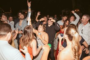 Crowd of wedding guests dancing and raising hands during lively reception party.