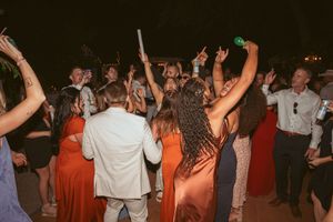Wedding guests dancing enthusiastically at a lively reception with people in orange dresses and formal attire.