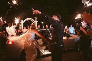 A sparkler sendoff illuminates a couple entering their car at a nighttime celebration.