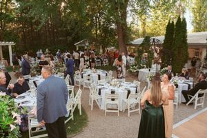 Guests enjoying an elegant outdoor wedding reception under trees with white chairs and tables at dusk.