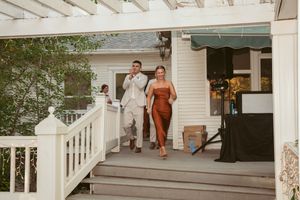 Two people in formal attire walk down white wooden steps at an outdoor venue.