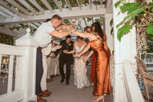 Wedding reception guests form dance line under white pergola.